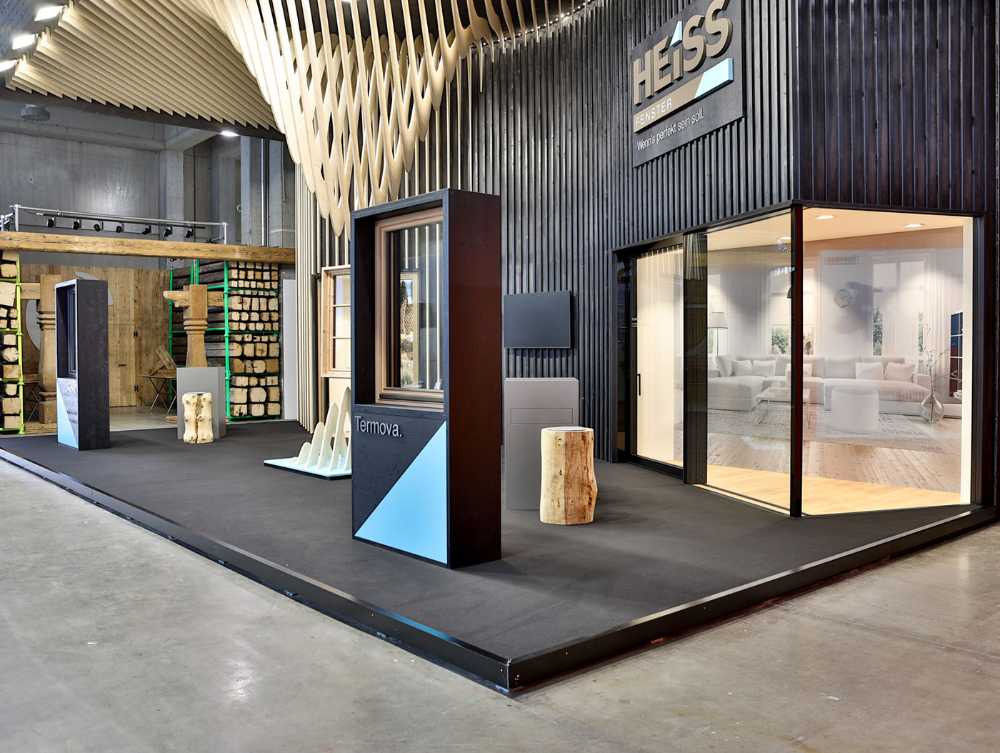 Modern custom trade show exhibit booth featuring sleek black walls, glass meeting space, wood accents, and branded display structures in a spacious expo hall.